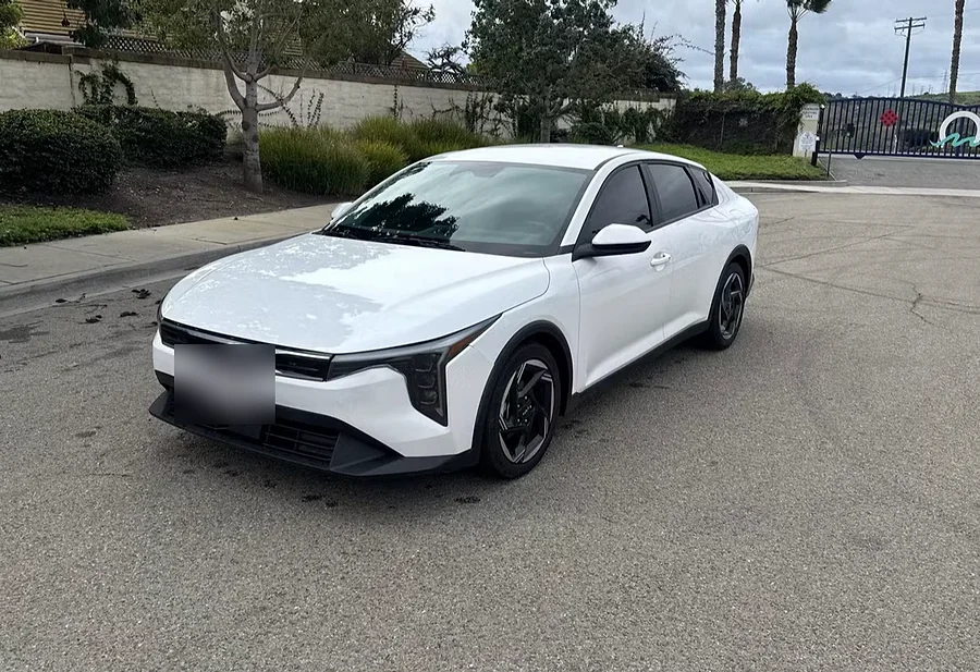 White Kia K4 sedan photographed from the front three-quarter angle